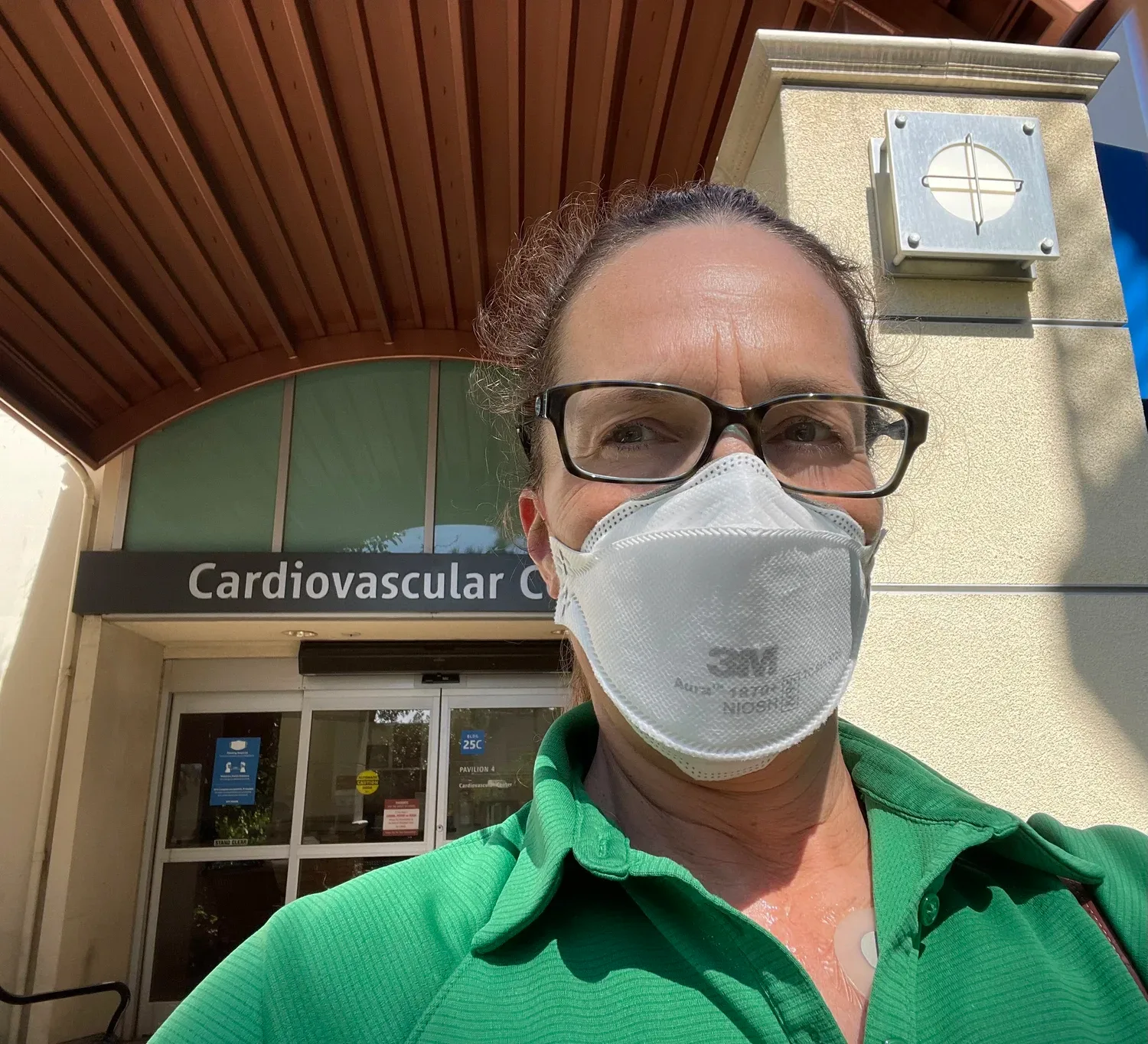 A middle-aged woman is wearing a mask outside a healthcare facility for cardiovascular issues.
