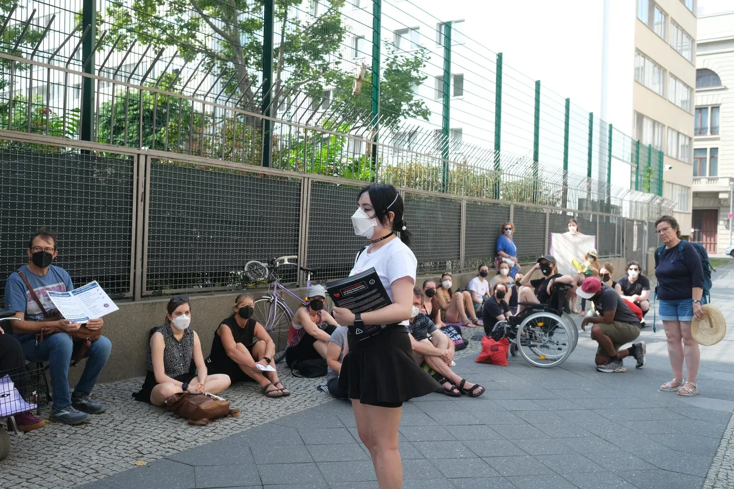 A Berlin Buyers Club member speaks to protesters sitting along a fence on a Berlin street, some of them in wheelchairs.