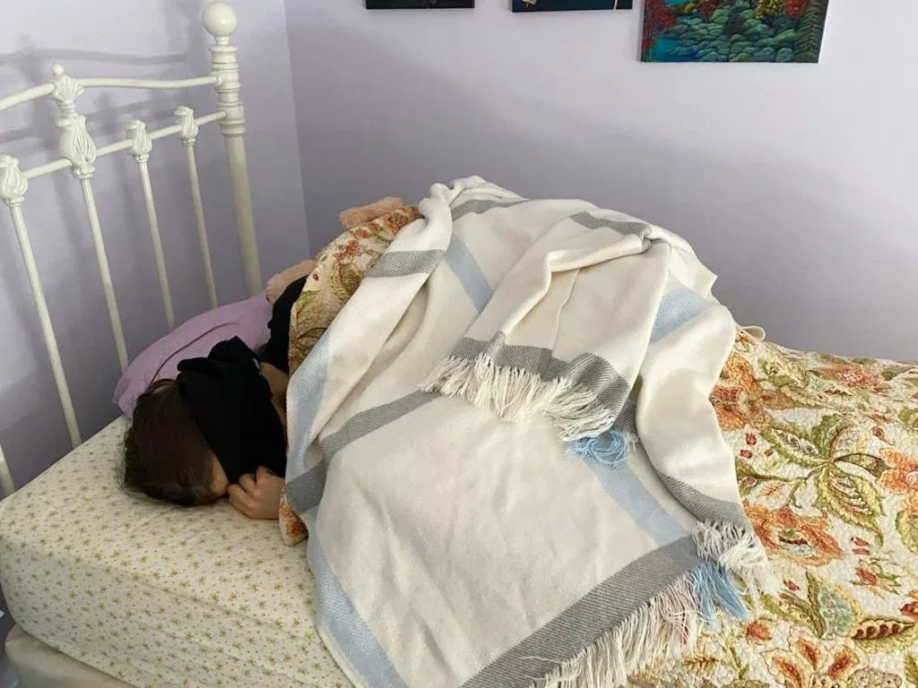 Amy, a young woman, is in bed with clothing covering her eyes, due to extreme light sensitivity.