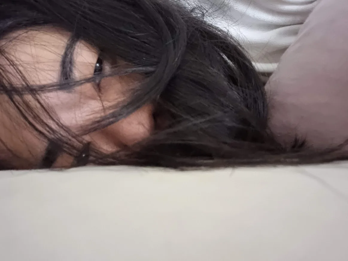 A young woman is lying down, looking into the camera with sadness in her eyes because she is so fatigued.