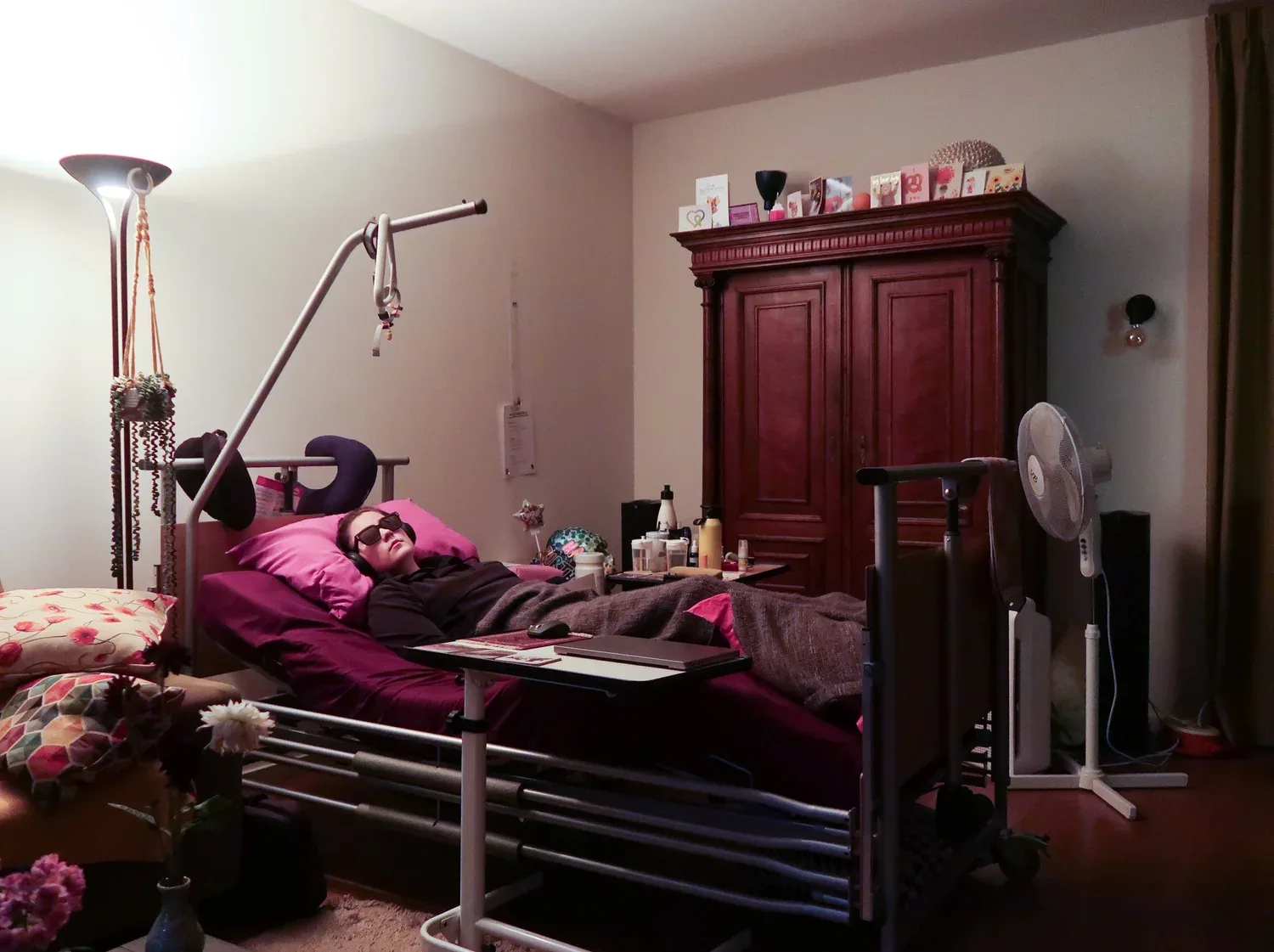 A young woman in her 20s is lying in bed, with sunglasses on due to light sensitivity.