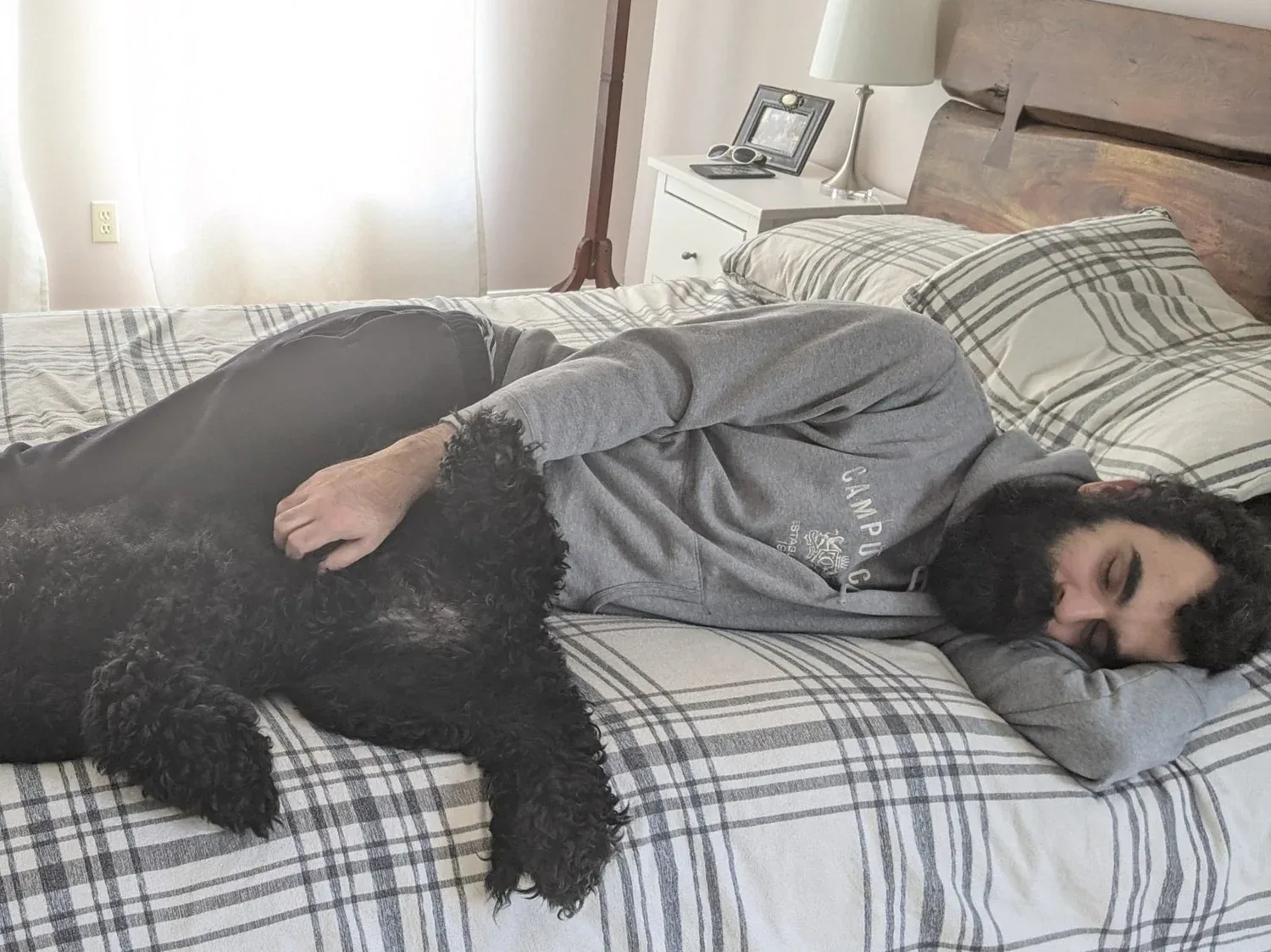 A man is lying in his bed next to his dog, exhausted.