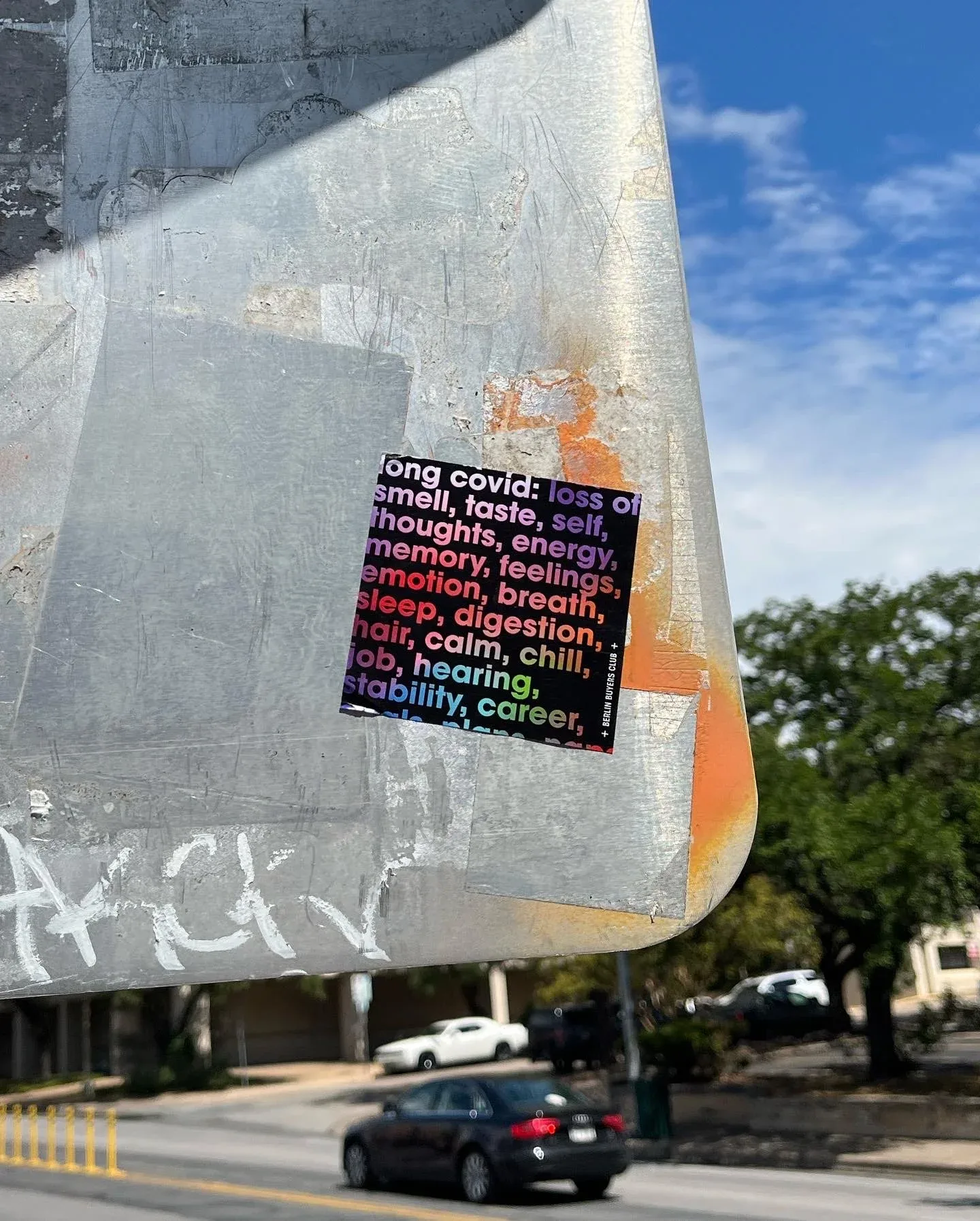 A Long Covid sticker on a lamppost in the sun: loss of smell, taste, self, thoughts, energy, memory, feelings