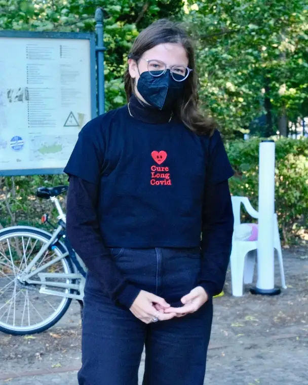 Person in a mask and a Cure Long Covid t-shirt standing in a park