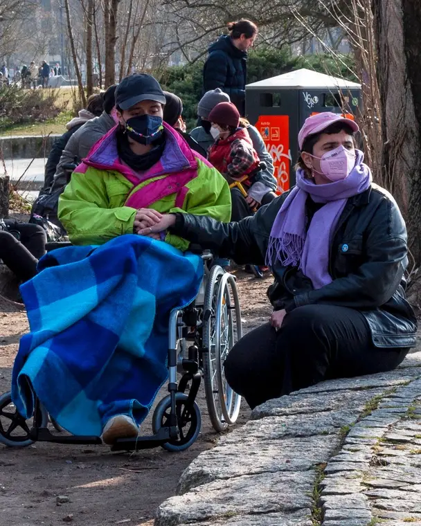 Protesters in masks at Mauerpark, one in a wheelchair under a blanket