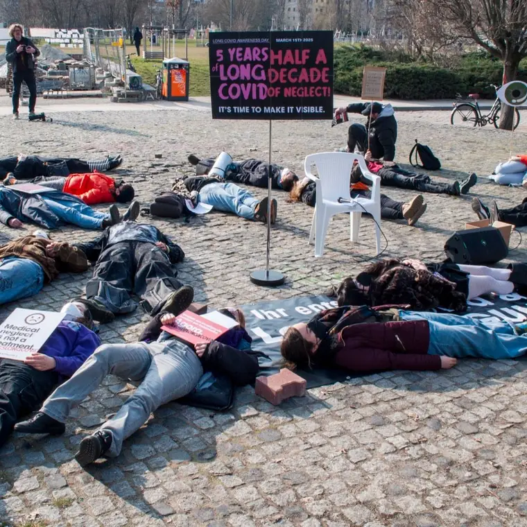 Die-in: people lying on the ground at Mauerpark beside a sign marking five years of Long Covid