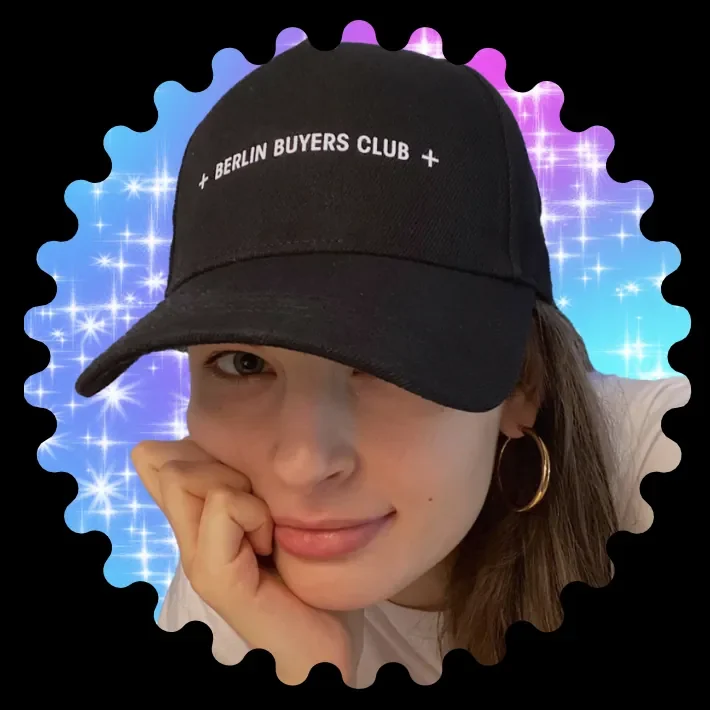 A woman in a black Berlin Buyers Club cap resting her chin on her hand, framed by blue and pink sparkles